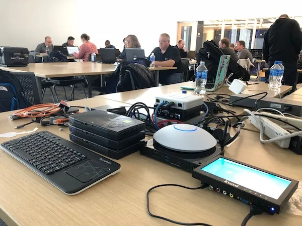 The original OpenSOC kit on a classroom table: stacked NUCs, a Ubiquiti access point and a small monitor
